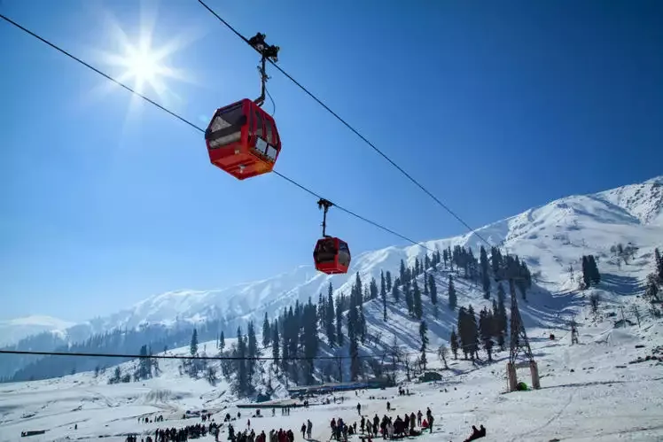 Red cabins of the Gulmarg Gondola gliding over snow slopes and pine forest